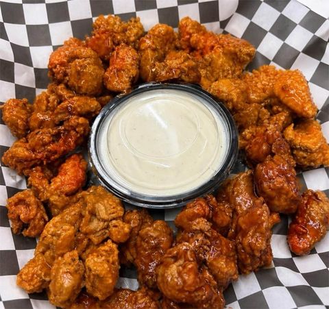 A basket of sauced chicken wings around a cup of ranch dressing